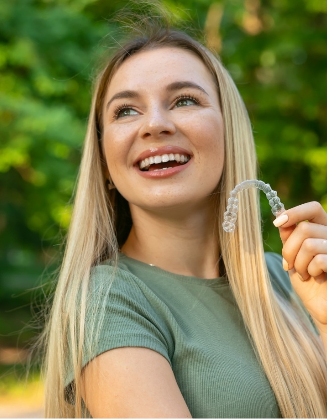 Smiling blonde woman holding an Invisalign clear aligner