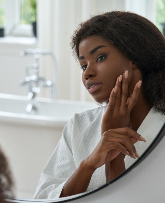 Woman touching her face while looking in mirror