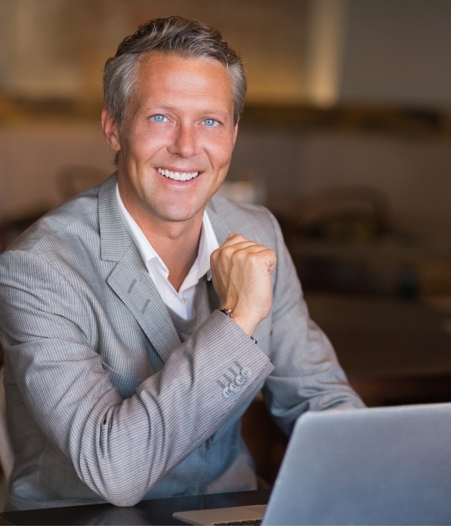 Smiling man in gray suit sitting at desk with laptop