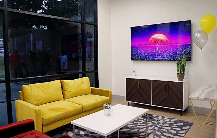 Reception area with yellow loveseat and large T V screen on wall