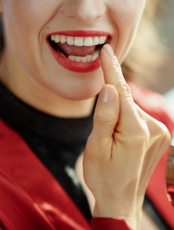 Woman with red lipstick pointing to her smile