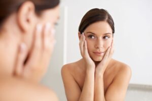 Woman looking in mirror, considering the appearance of her skin